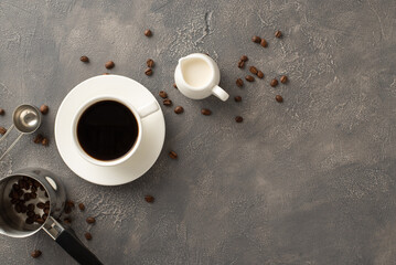 Café Creation: Top-down view of coffee beans, espresso cup, cream jar, coffee turk, measuring spoon on textured grunge backdrop with empty space for promo message