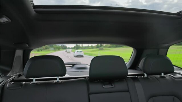 Beautiful rear view interior with leather seats and panoramic sunroof of new black electric car driving on highway. Sweden.