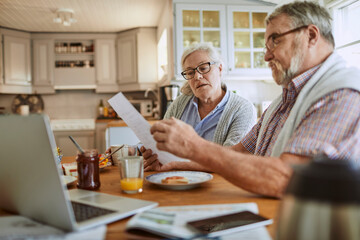 Senior Caucasian couple going over their bills and home finances in the morning in the kitchen