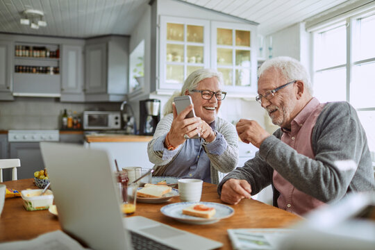 Senior Caucasian couple using a smartphone while having breakfast together in the kitchen in the morning