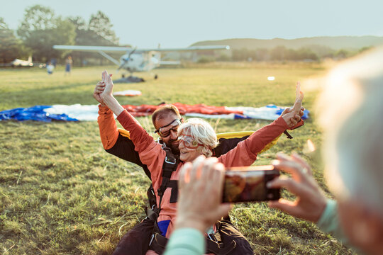 Senior man taking a picture of his wife after landing from a skydive with her skydiving instructor