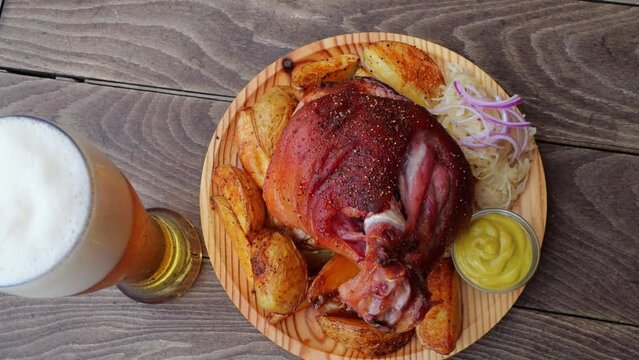 Roasted pork knuckle with potatoes, sauerkraut and beer rotate on a wooden surface. Top view. Close up. Outdoor. Oktoberfest