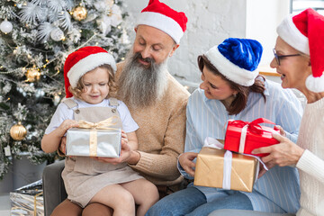 Grandmother, grandfather, daughter and granddaughter celebrating holidays at home together. Happy smiling family near beautiful Christmas new year tree exchanging gifts in the morning