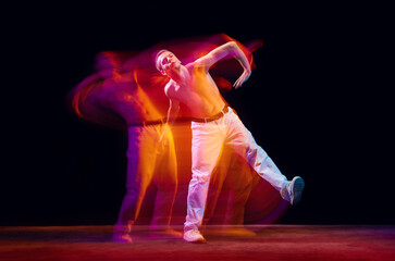 Fototapeta premium Inspiration and freedom. Young shirtless guy making chaotic movements against black studio background in neon with mixed lights effect. Concept of movements, art, dance and sport, fashion, youth, ad