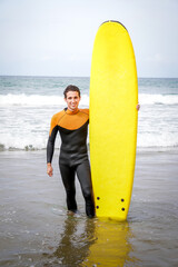 Vertical Portrait of Young Adult Surfer Smiling at Camera While Holding His Board with Neoprene Standing on the Seashore