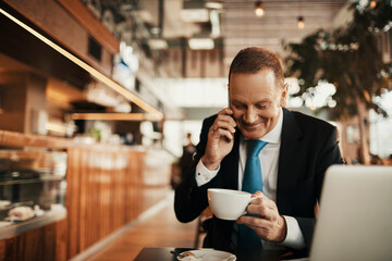 Middle aged businessman talking on the smartphone while drinking coffee in a cafe