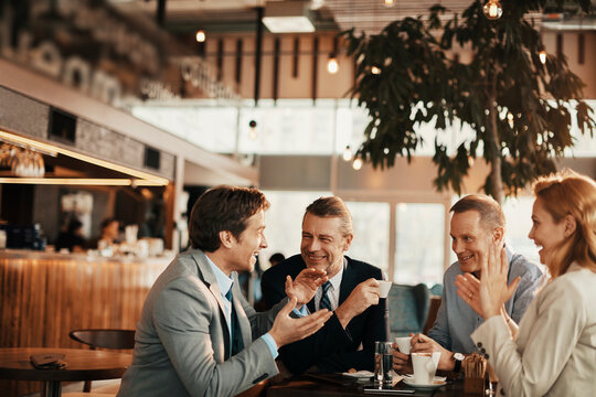 Group Of Middle Aged Business Coworkers Having A Meeting Over Coffee In A Cafe Decorated For Christmas And The New Year Holidays