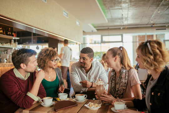 Young and diverse group of people talking while having coffee together in a cafe