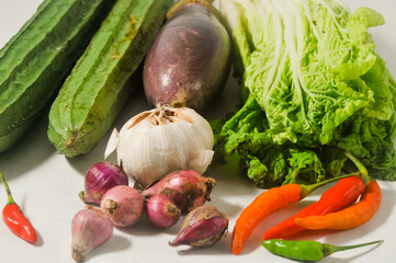Two luffa gourd or oyong or gambas, a purple eggplant, a white mustard and garlics, onions, chilies isolated on a white background.