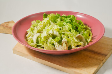 Chopped Chinese cabbage in a red plastic plate on a wooden cutting board isolated on a white background.