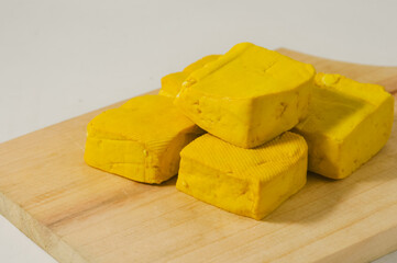 Five yellow tofus on a wooden cutting board isolated on a white background