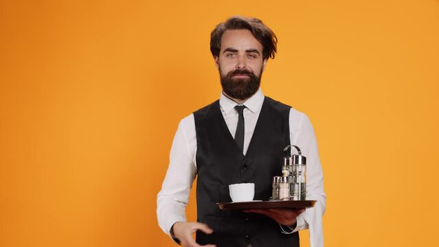 Elegant butler having new idea on camera, raising index finger and indicating upwards direction with restaurant food tray in hand. Skilled waiter feeling genious, innovative with fresh thoughts.