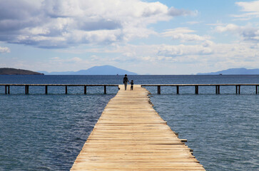 Mother and son walking on a wooden pier background with blue sky and white clouds