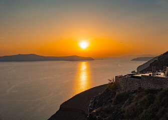 Santorini, Greece - 05 25 2023: Thira (Fira) sunset view from the volcanic island overlooking other smaller volcanic islets and an infinity pool