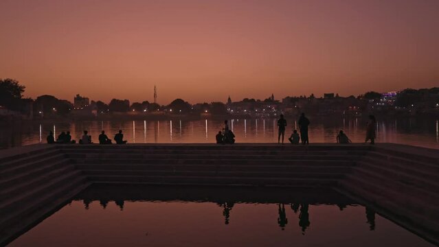 People sitting on the ghat of Pushkar Lake by the city at sunset