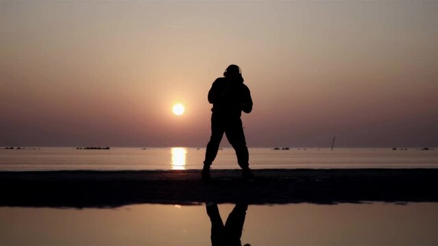 young boy kicking air with leg on the beach, on the sea, on the sunrise