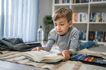 caucasian boy pupil student read book at home on the floor study learn