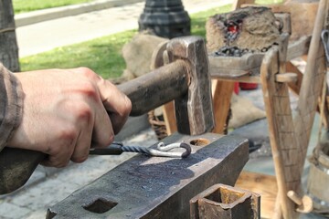 Close-up of authentic blacksmith working with hammer and iron at anvil of workshop. Traditional manually forging of molten metal. Craftsman worker forges iron detail creation