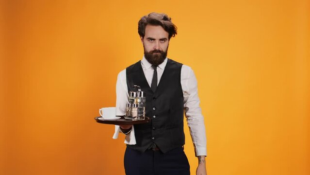 Skilled butler indicates stop sign with palm, posing against yellow background with food tray. Restaurant worker in suit showcasing rejection and dismissal, disagreeing with something.