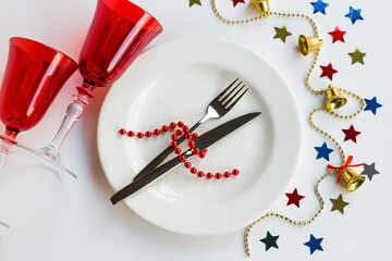 Christmas design on white surface, with empty white plate, red glass and decorative ornaments