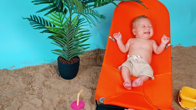 Tiny Caucasian infant lying in the baby chair starting to cry. Newborn boy resting in the beach.