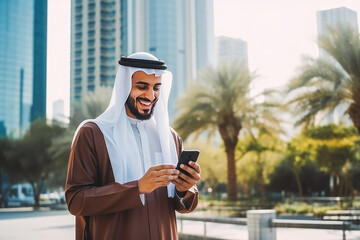 Handsome young arabic man standing outside in city park with a mobile phone in his hand and smiling