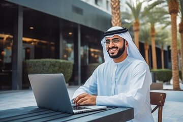 Handsome smiley young male arabic office assistant working remotely on her computer outside the coffee shop