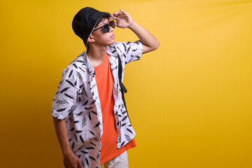 Fototapeta premium Young Asian man wearing casual beach clothes standing over yellow background looking far away with hand over head. Searching concept