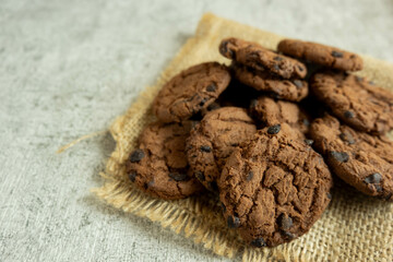 A pile of chocolate cookies with chocolate chips on top, on a textured gray table