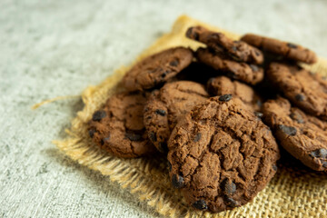 A pile of chocolate cookies with chocolate chips on top, on a textured gray table