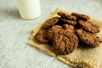 A pile of chocolate cookies with chocolate chips on top, on a textured gray table