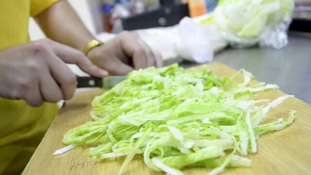 Joven cocinero cortando vegetales frescos, picando lechuga en la cocina. 