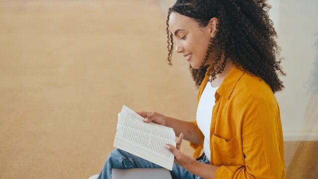Side view photo of a lovely stylish curly haired brazilian or hispanic female student, sit near the university campus, focused reading her favorite a book, preparing for the exam, smile