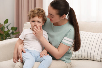 Mother applying ointment onto her son`s nose on sofa at home