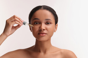 Obraz na płótnie Canvas Beautiful woman applying serum onto her face on white background