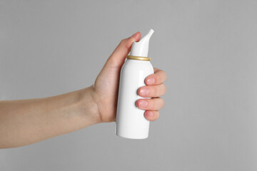 Woman holding nasal spray on grey background, closeup