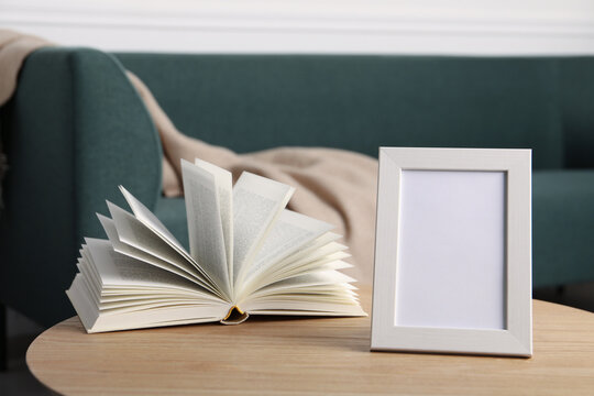 Empty square frame and book on wooden table indoors