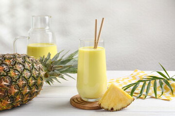 Tasty pineapple smoothie and fruit on white wooden table