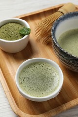 Fresh matcha tea, bamboo whisk and green powder on wooden tray, closeup