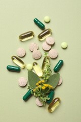 Different pills and herbs on light green background, flat lay. Dietary supplements