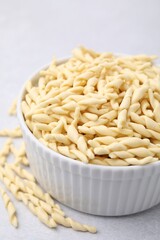 Bowl with uncooked trofie pasta on light grey table, closeup
