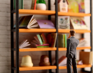 Miniature scene of a businessman looking at a large shelf of stacked books. One book on the shelf is blank.