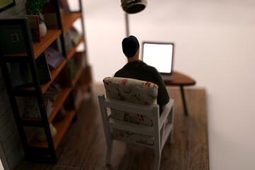 Miniature scene of a man sitting in a chair in a room looking at the blank screen of a laptop computer.