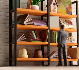 Miniature scene of a businessman looking at a large shelf of stacked books. One book on the shelf is blank.