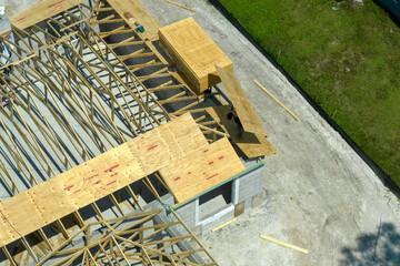 Builders working on roof construction of unfinished residential house with wooden frame structure in Florida suburban area. Housing development concept