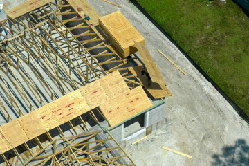 Builders working on roof construction of unfinished residential house with wooden frame structure...