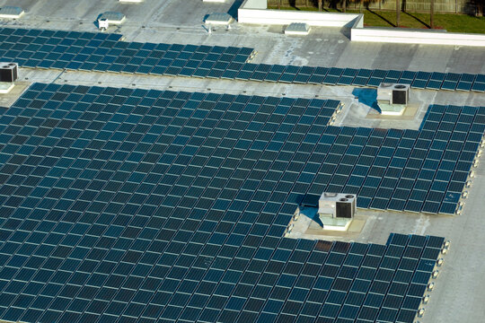 Production of sustainable energy. Aerial view of solar power plant with blue photovoltaic panels mounted on industrial building roof for producing green ecological electricity
