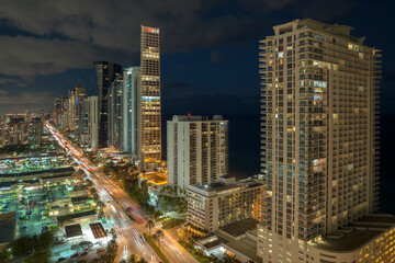 Fototapeta na wymiar View from above of brightly illuminated city street with dense traffic and high skyscraper buildings in downtown of Sunny Isles Beach in Florida, USA. American tourist urban district at night