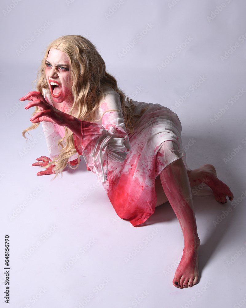 Wall mural  portrait of  scary vampire zombie bride, wearing elegant halloween fantasy costume with bloody red paint splatter in  angsty crouching sitting pose. Isolated on studio background  - Wall murals