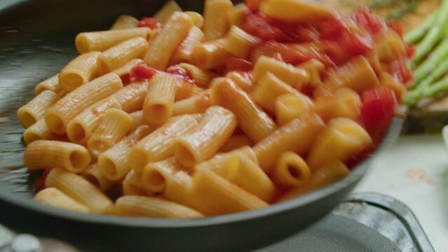 Tossing rigatoni with tomato sauce in a skillet while cooking delicious pasta. Extreme close-up shot in slow mo